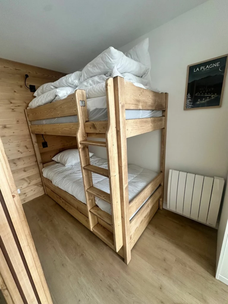 Coin nuit avec lits superposés en bois adaptés aux adultes et affiche vintage de La Plagne