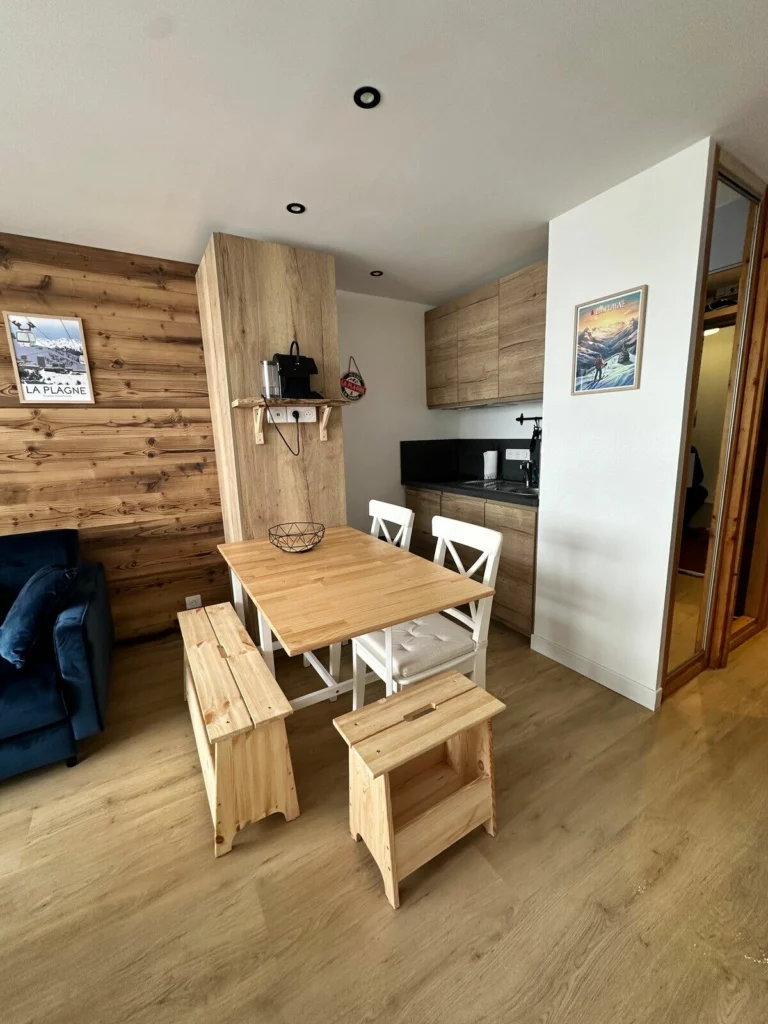 Coin repas avec table en bois massif, banc et chaises blanches, face à la cuisine