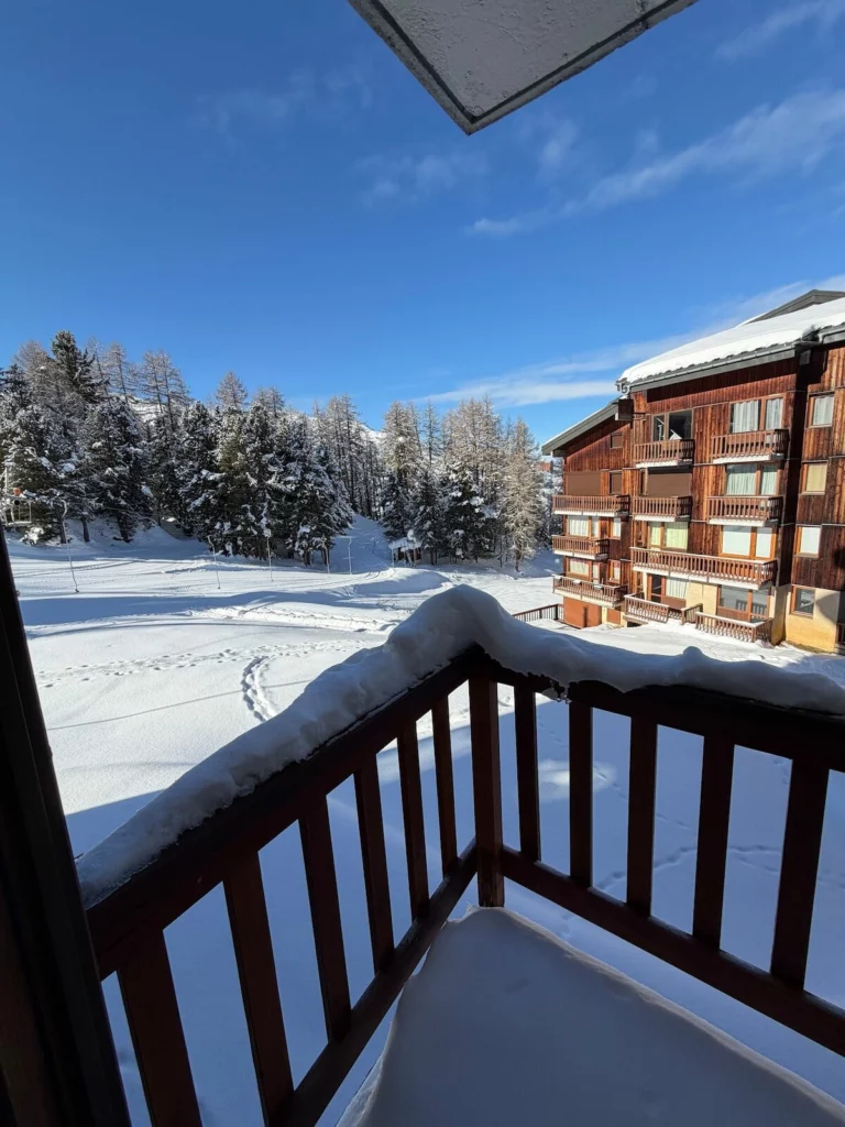 Vue depuis le balcon de l'appartement Grande Rochette : sapins enneigés et résidence voisine sous le soleil
