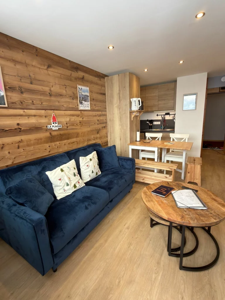Séjour chaleureux avec mur en bois clair, canapé en velours bleu nuit et table basse en bois